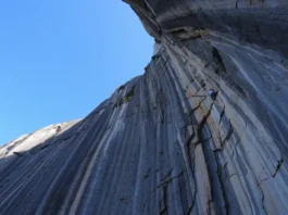 A massive, sunlit limestone cliff, showcasing the world's hardest climbing route under a clear blue sky, conveying extreme difficulty and challenge.