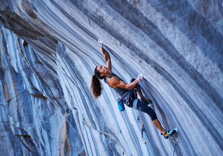 Elite climber executing a dynamic move on a severely overhanging 9c sport climbing route, showcasing the pinnacle of difficulty on the world's hardest climbs.