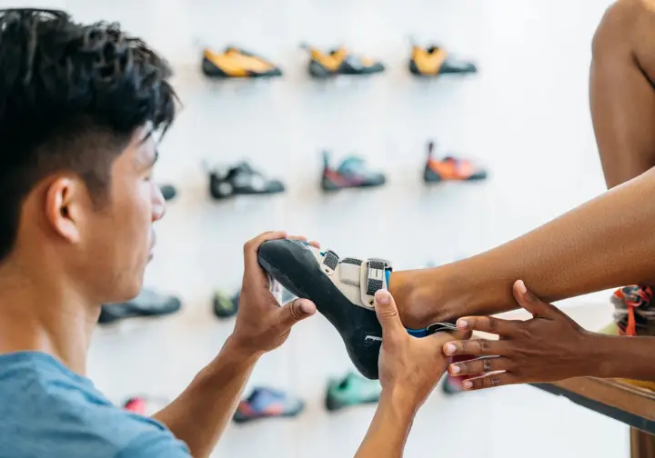 Diverse hands examining a climbing shoe on a foot, demonstrating the core principles of understanding how a climbing shoe should fit for optimal performance.