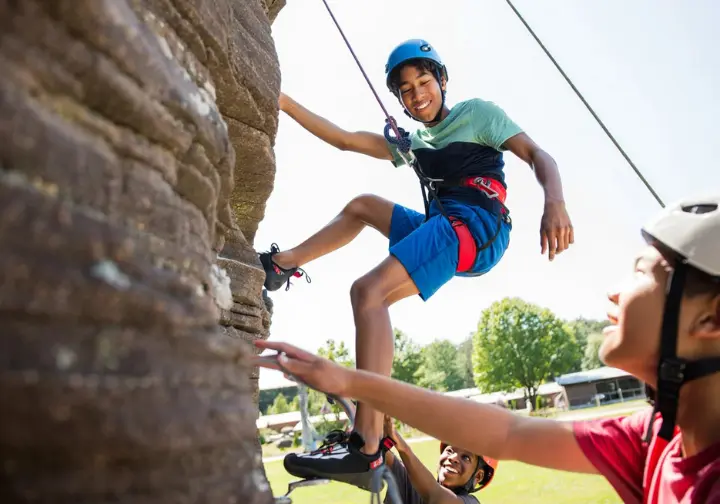 Teenager confidently rock climbing outdoors, illustrating the benefits of choosing a rock climbing sleepaway camp.