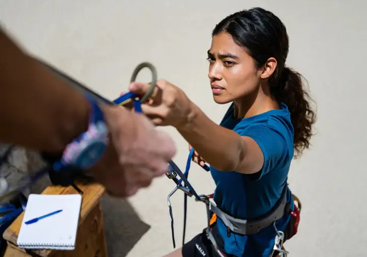 A climber inspecting their harness with a checklist nearby, demonstrating how to master harness inspection for safety and to understand how long a climbing harness lasts.