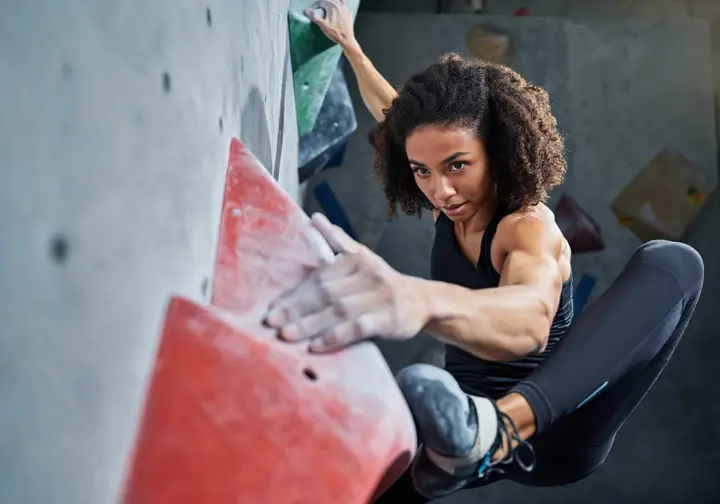 Female climber executing a precise bouldering technique on a gym wall, showcasing how mastering movement helps to get better at bouldering.
