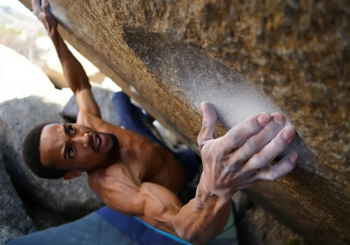 Boulderer demonstrating incredible power and precision on tiny granite holds of a V17 problem, representing the apex of bouldering difficulty on the world's hardest routes.