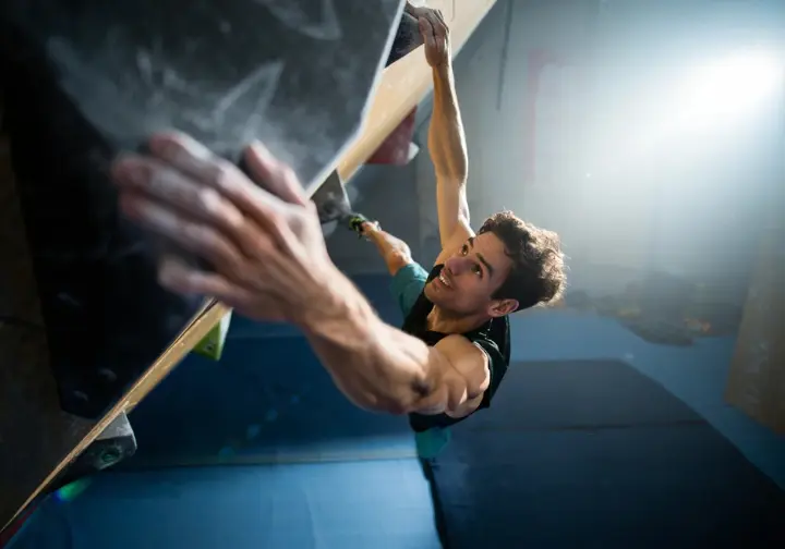 White male climber demonstrating biomechanical implications of ape index with a long reach on an overhanging bouldering problem.