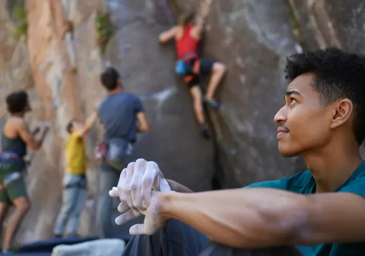 Climber reflecting at a crag, with diverse climbers in background, showing ape index in the broader context of rock climbing, beyond the tape measure.