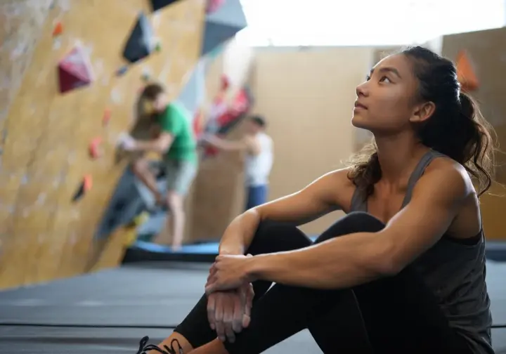 Female climber mentally strategizing at the base of a bouldering wall, highlighting the mental game for success in getting better at bouldering.