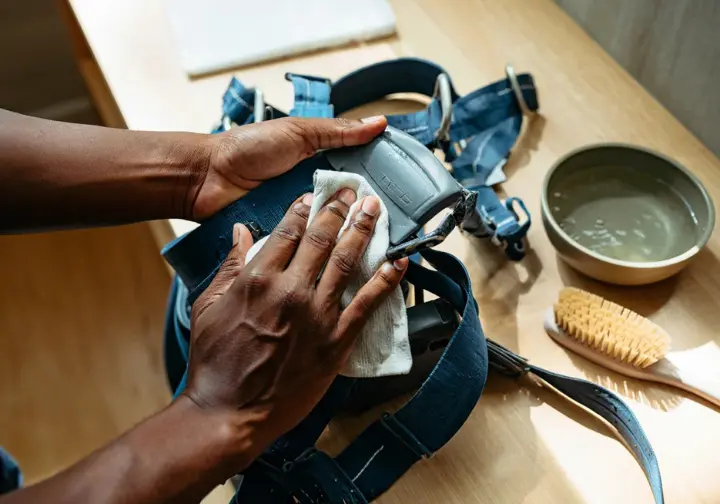Climber's hands carefully cleaning a climbing harness, demonstrating proper care and maintenance to extend its life, a key factor in how long a climbing harness lasts.