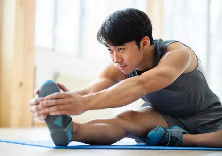 Asian male climber performing a recovery stretch, emphasizing injury prevention for sustainable progress in getting better at bouldering.