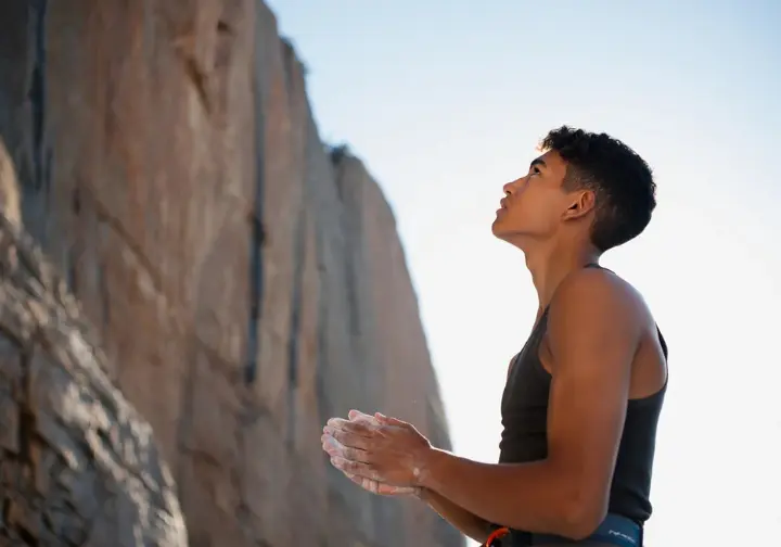 Young, diverse climber gazing up at a massive, unclimbed cliff, symbolizing the future of hard climbing and the next generation tackling the world's hardest routes.