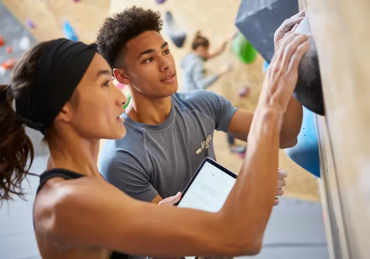 Two diverse climbers discussing a bouldering problem, illustrating the continuous improvement loop of learning and adapting to get better at bouldering