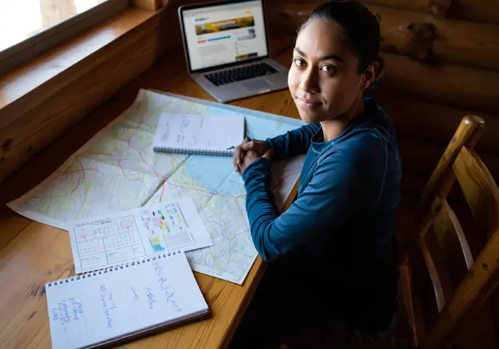 Planning the Mount Whitney Mountaineer's Route ascent: climber with maps, calendar, and notes detailing logistics and timing.