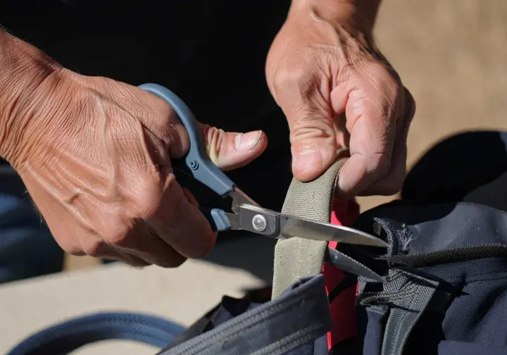Hands cutting a retired climbing harness to render it unusable, illustrating responsible disposal and the end of how long a climbing harness lasts.