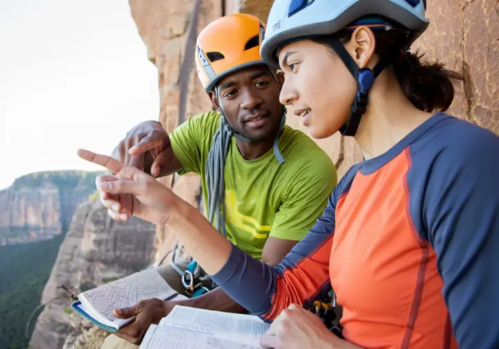Two diverse trad climbers discussing route and safety on a multi-pitch climb, highlighting judgment in what is trad climbing.