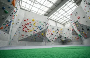 All Parts of a Climbing Wall: From Frame to Holds A wide overview of a modern climbing gym, highlighting the different parts of a climbing wall, including the safety flooring, textured panels, various holds, and top rope anchors.