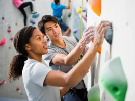 Learn how to rock climb safely: diverse instructor guiding a beginner on their first climb in a gym.
