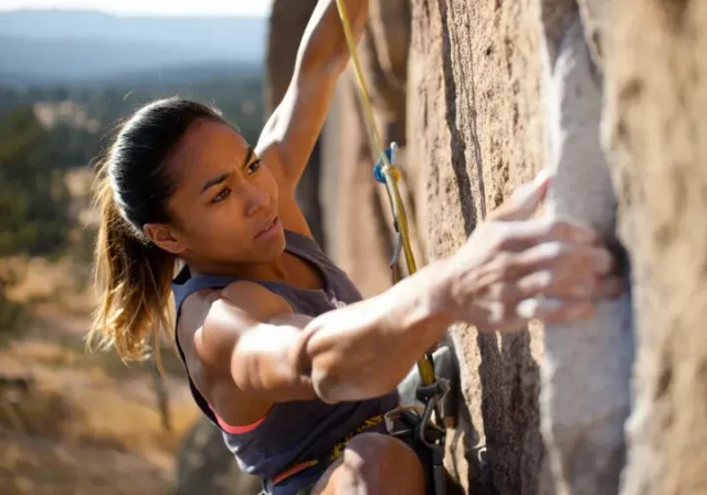 Master strength exercises for climbing: diverse female climber powerfully moving on a steep outdoor route to climb harder.