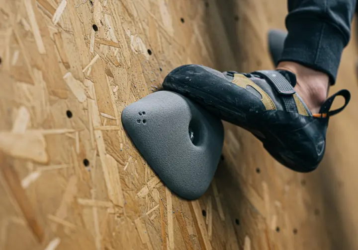 A close-up of a climbing wall's textured panel surface, with a climber's shoe smearing on it to show the friction an essential part of the climbing surface provides.