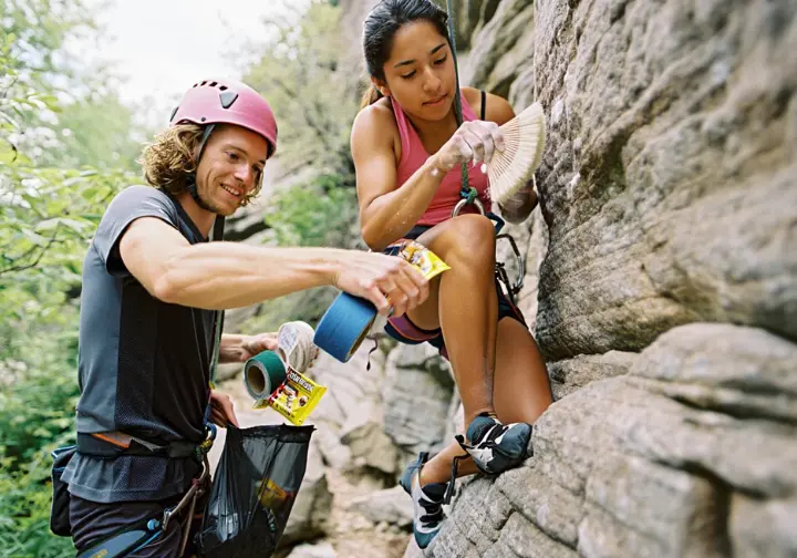 Conquering the crag with outdoor rock climbing ethics: climbers practicing Leave No Trace by brushing holds and packing out trash.