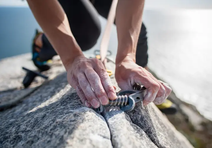 Mastering trad & sea cliff climbing in Maine: close-up of hands placing gear on a granite sea cliff.