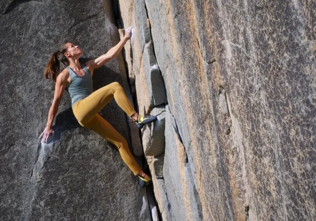 Woman rock climbing outdoors in durable and comfortable women's climbing pants, showcasing style meeting function.