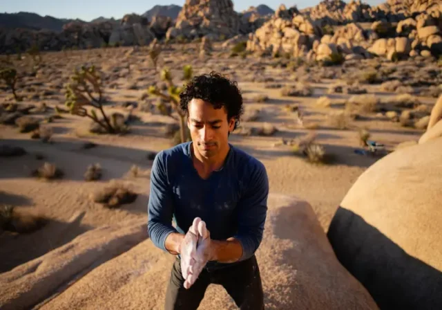 Male climber intently studying a large granite boulder in Joshua Tree National Park at golden hour, representing a definitive guide to joshua tree bouldering.