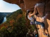New River Gorge Rock Climbing: Pro Beta & Areas Climber leading a route on Nuttall Sandstone with the New River Gorge Bridge in the background, for a guide on rock climbing New River Gorge pro beta and areas.