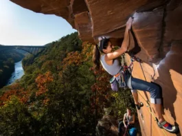 Climber leading a route on Nuttall Sandstone with the New River Gorge Bridge in the background, for a guide on rock climbing New River Gorge pro beta and areas.