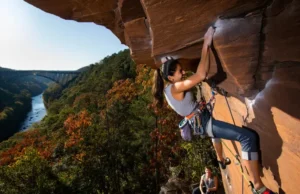 New River Gorge Rock Climbing: Pro Beta & Areas Climber leading a route on Nuttall Sandstone with the New River Gorge Bridge in the background, for a guide on rock climbing New River Gorge pro beta and areas.