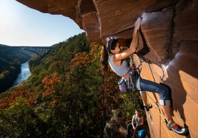 Climber leading a route on Nuttall Sandstone with the New River Gorge Bridge in the background, for a guide on rock climbing New River Gorge pro beta and areas.