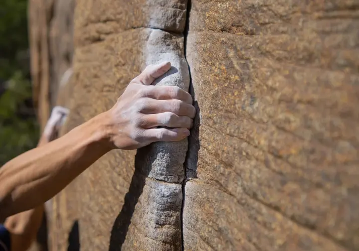 Close-up of Nuttall Sandstone with a climber's hand, detailing the rock type for New River Gorge rock climbing.