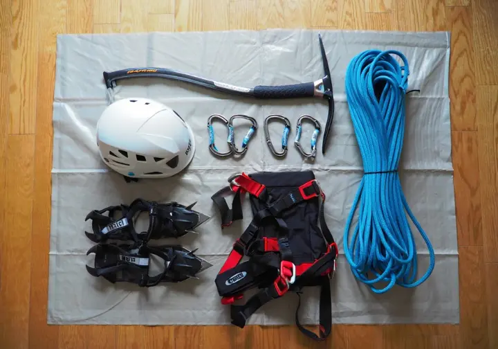 Essential gear for mountain climbing: Flat lay of ice axe, crampons, helmet, harness, rope, and carabiners.