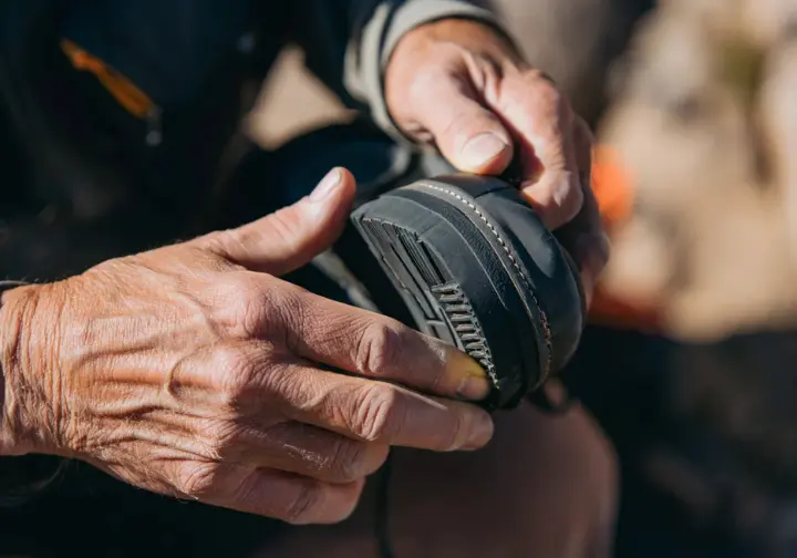 Critical choices deep dive: Hands inspecting the sole stiffness and heel welt of a mountaineering boot for crampon compatibility.