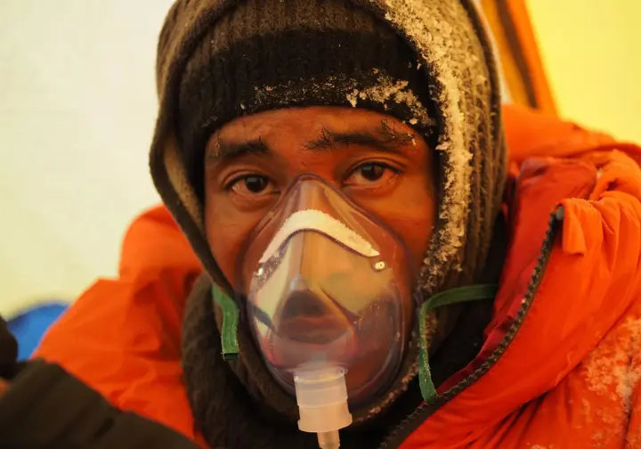 Physiological toll above 8000m: Close-up of a fatigued climber wearing an oxygen mask inside a tent at Everest Camp 4.