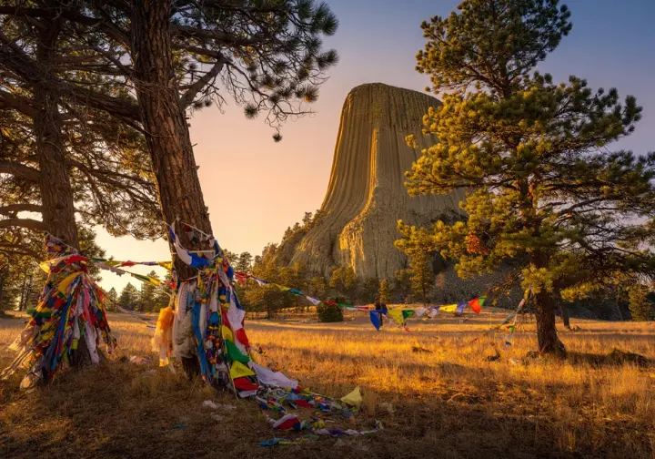 Climbing Devils Tower, Wyoming with reverence: Native American prayer flags in foreground with the sacred Tower at sunset, highlighting cultural respect.