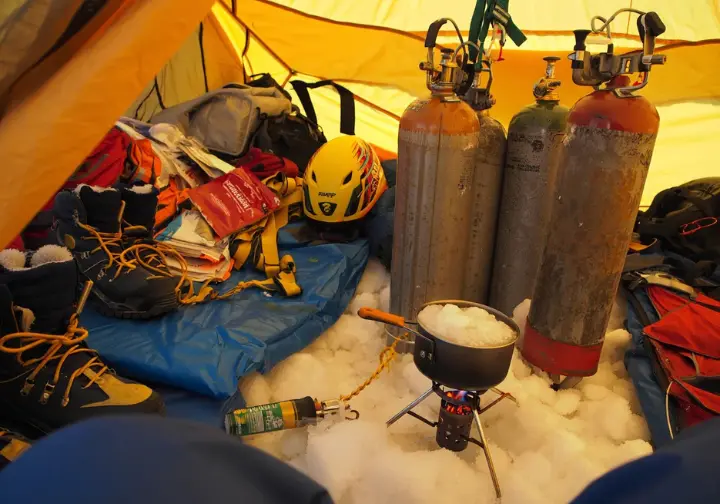 Logistics at Camp 4 Everest: Interior of a tent showing oxygen cylinders, stove melting snow, food, and gear preparations.