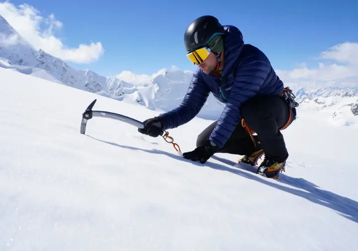 Understanding the Seven Summit challenge: Mountaineer training with an ice axe on a steep snow slope, representing preparation.