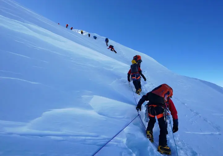 Navigating extreme dangers: Climbers carefully ascending a steep, exposed section with fixed ropes high on Mount Everest above Camp 4.