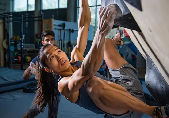 Climber engaged in specific, intense training for Freerider's required skills on a specialized indoor climbing wall, with a partner spotting.