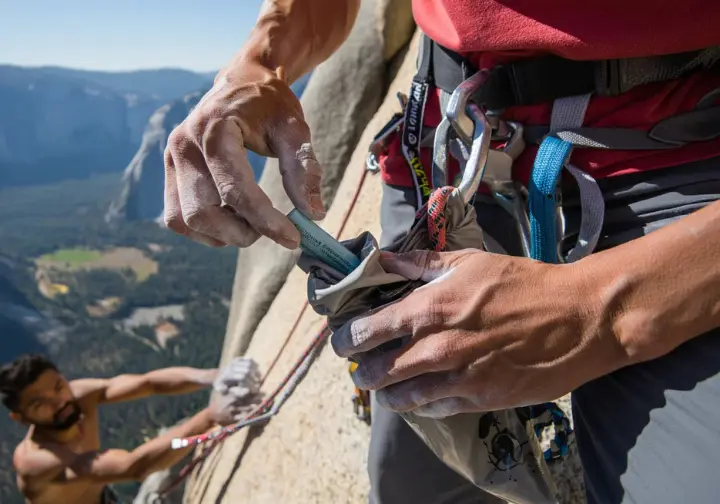 Climber responsibly packing out waste into a wag bag on an El Capitan bivy ledge, illustrating sustainable climbing ethics and environmental responsibility on Freerider.