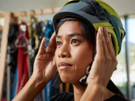 Climber carefully adjusting the fit of a climbing helmet in a gear shop, emphasizing the importance of choosing the right helmet fit because your head matters.