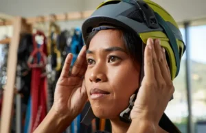 Your Head Matters: Choose Right Climbing Helmet Fit Climber carefully adjusting the fit of a climbing helmet in a gear shop, emphasizing the importance of choosing the right helmet fit because your head matters.
