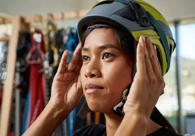 Climber carefully adjusting the fit of a climbing helmet in a gear shop, emphasizing the importance of choosing the right helmet fit because your head matters.