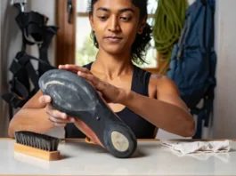A climber carefully inspecting the rubber on her climbing shoe, with odor-control and cleaning tools nearby, demonstrating comprehensive shoe care to extend its life.