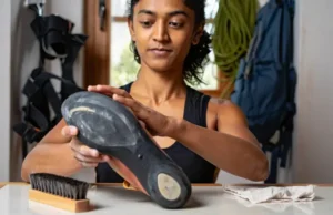 Mastering Climbing Shoe Care: Odor, Rubber & Life A climber carefully inspecting the rubber on her climbing shoe, with odor-control and cleaning tools nearby, demonstrating comprehensive shoe care to extend its life.