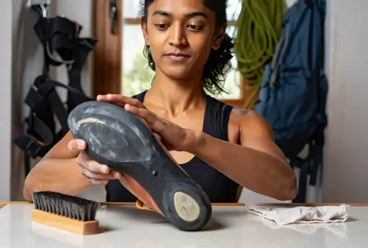 A climber carefully inspecting the rubber on her climbing shoe, with odor-control and cleaning tools nearby, demonstrating comprehensive shoe care to extend its life.
