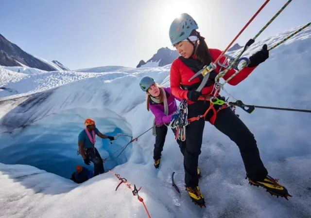 Alpinist team performing a crevasse rescue practice on a heavily crevassed glacier, using ropes, ice axes, and a hauling system, highlighting critical glacier travel and rescue skills.