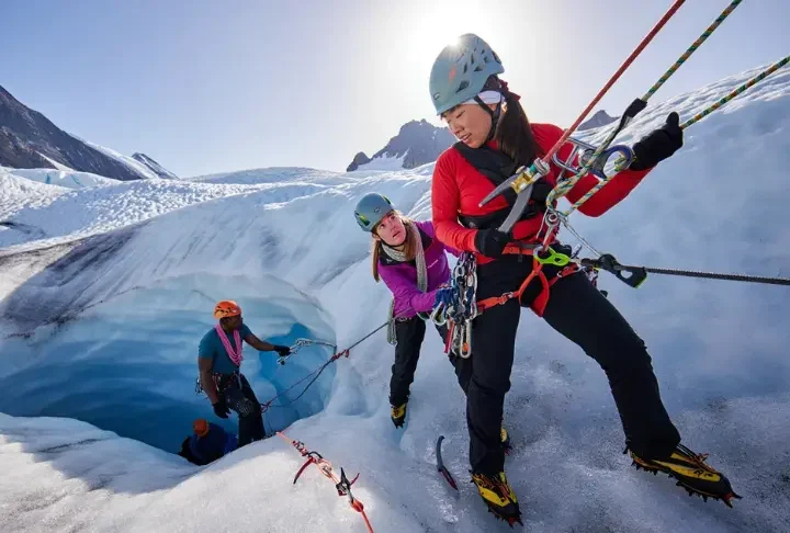 Alpinist team performing a crevasse rescue practice on a heavily crevassed glacier, using ropes, ice axes, and a hauling system, highlighting critical glacier travel and rescue skills.