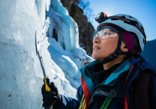 Experienced ice climber intently decoding complex ice formations and conditions on a frozen waterfall, planning safe ascent strategies with ice tools and gear.