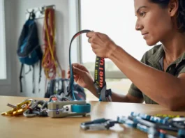 A female climber performing a crucial check by inspecting her climbing harness, with carabiners and other hardware laid out for maintenance.