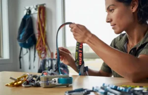 Hardware & Harness Maintenance: The Crucial Checks A female climber performing a crucial check by inspecting her climbing harness, with carabiners and other hardware laid out for maintenance.